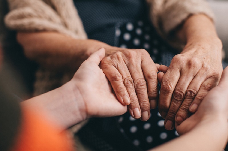 A close up of hands; a family member holding hands with an older family member for support.