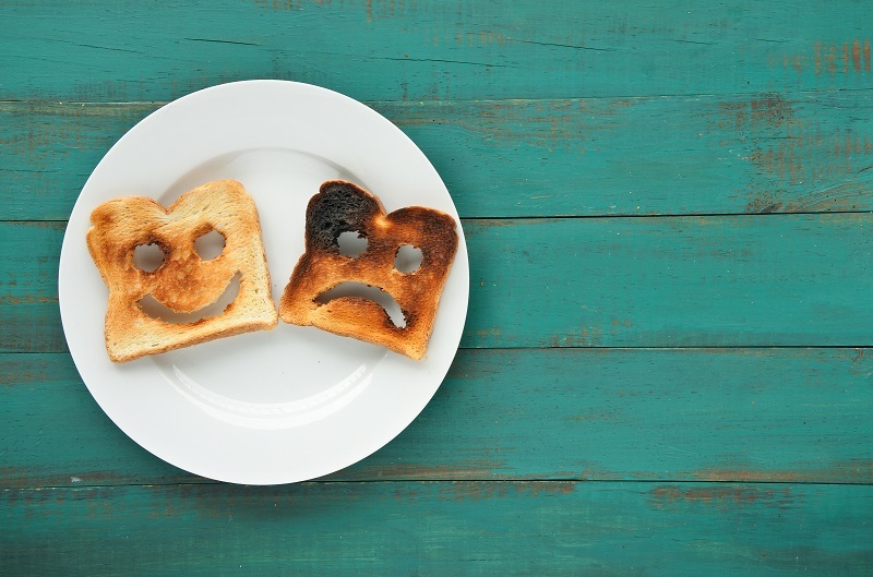 Flat lay view of two slices of toasted bread on a white plate; one has a happy face, and the other is sad.